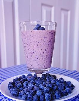 blueberry smoothie in a glass cup surrounded by blueberries